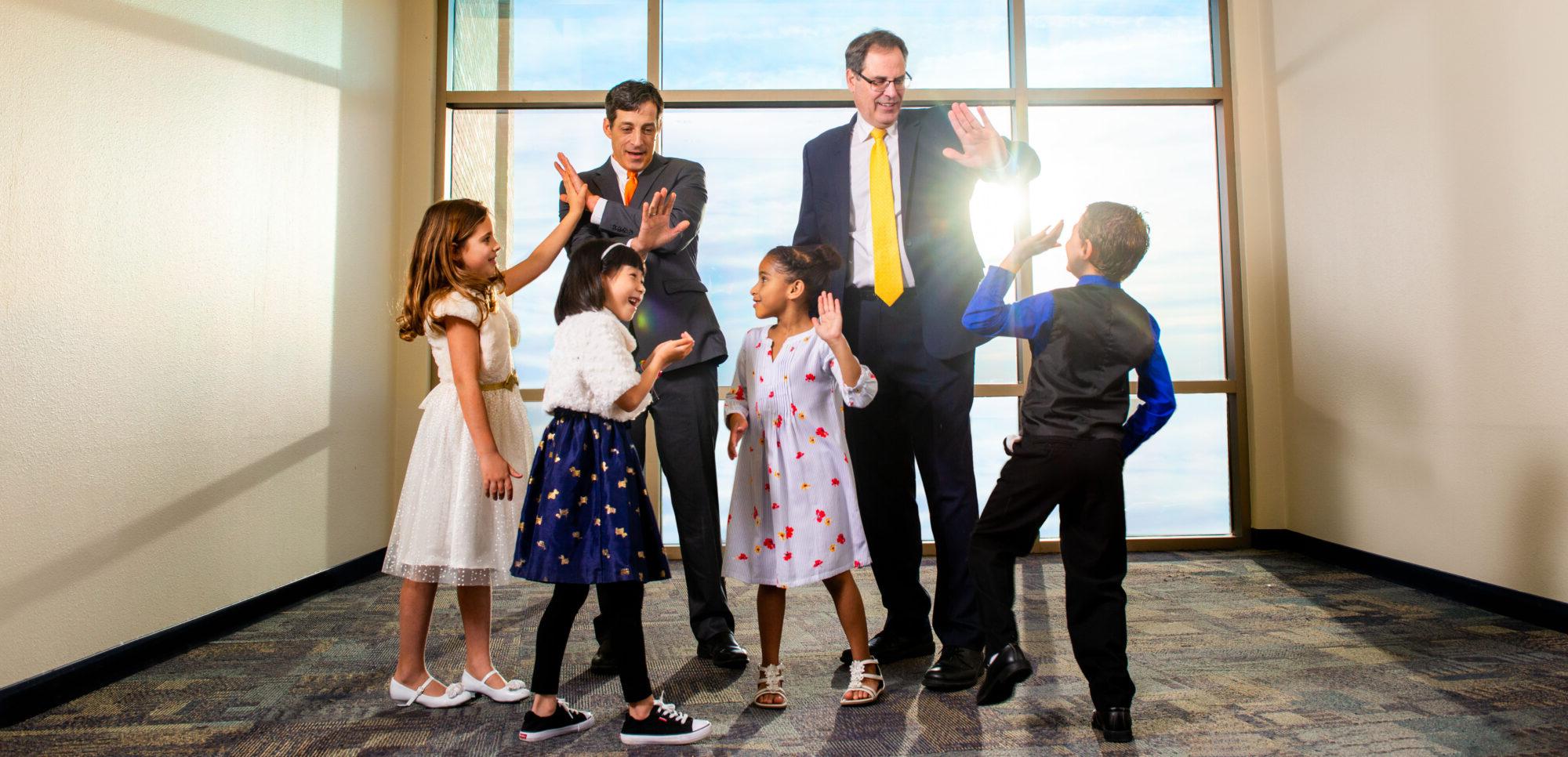 Two men giving four kids high fives.