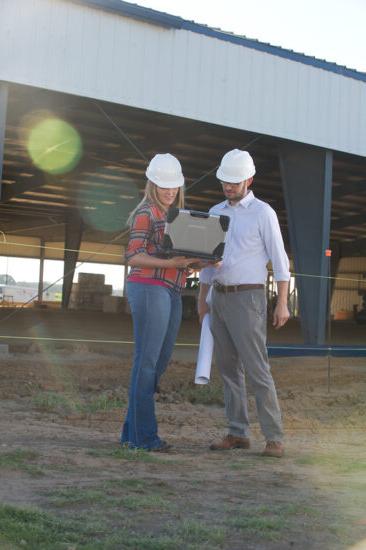 A male and female wearing plastic caps looking at a laptop in front of a building