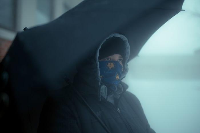 A TAMUC student under an umbrella, bundled up and looking out at the snow